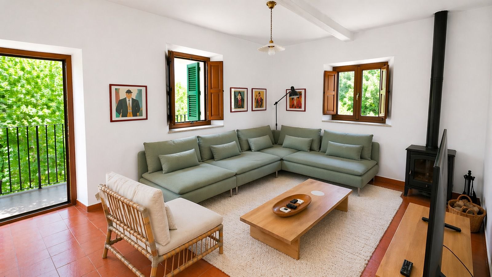 Lichte woonkamer van het vakantiehuis met sage groene hoekbank, originele terracotta tegelvloer, witte muren en zwarte houtkachel